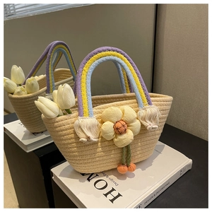 Close-up of handmade straw tote with rainbow handle and yellow flower charm on books