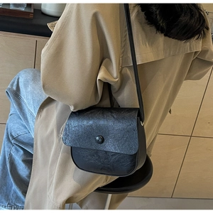 Close-up of black retro saddle bag on model wearing trench coat in minimalist interior