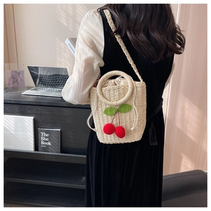 Detail of beige woven bucket bag featuring plush red cherries and a drawstring lining