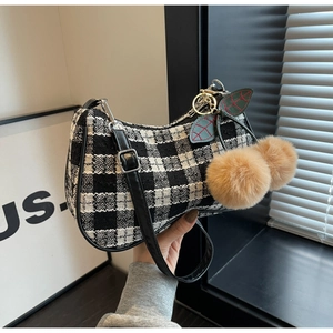 Close-up of black and white plaid hobo bag with leather trim and decorative fur pom-poms