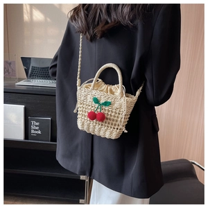 Detail of hand-woven straw bucket bag with knit cherry charm and drawstring closure