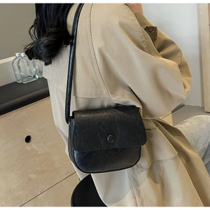 Detail view of the black retro textured crossbody bag worn by a model in a lifestyle setting