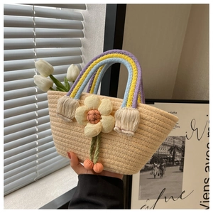 Detailed shot of handmade straw bag featuring rainbow woven handles and a 3D fabric sunflower