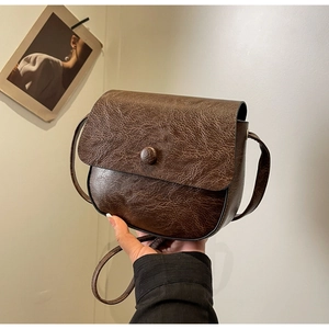 Detail of vintage dark brown crossbody bag featuring cracked leather texture and round buckle