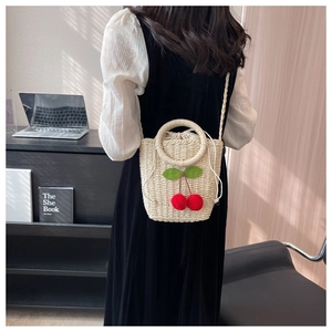 Detailed shot of handmade straw bag featuring 3D cherry decor and woven top handle