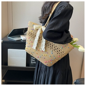 Détail du sac cabas en paille avec pompons colorés et un grand nœud en dentelle blanche