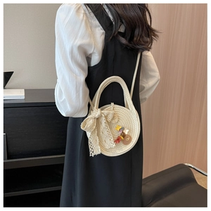 Vue détaillée du sac rond en paille crème avec nœud en dentelle et fleurs sur modèle