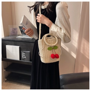 Detailed view of hand-woven straw bucket bag with cherry charms and drawstring closure