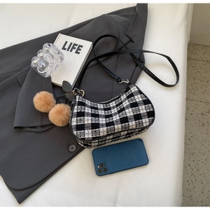 Detail of checkered baguette bag with plush cherry charm and sleek black leather strap