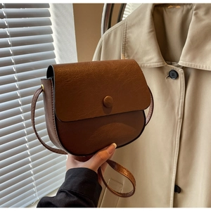 Close-up of vintage brown leather saddle bag with round buckle and adjustable strap