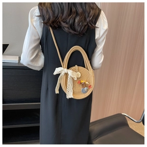 Détail d'un sac rond en paille avec nœud en dentelle blanche et breloques porté en bandoulière