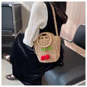 Detail of straw woven crossbody bag featuring red cherry decor and drawstring lining