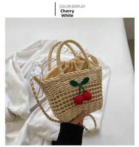 Detailed view of hand-woven straw bucket bag with red cherry accents and yellow drawstring