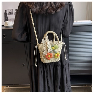 Detail of cream handmade woven straw bucket bag with lace bow and floral charms