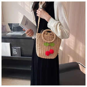 Detail of woven straw bucket bag with red cherry charms and drawstring linen liner