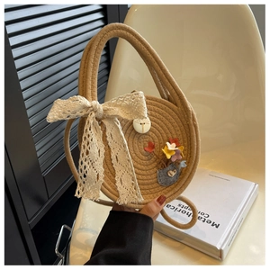 Détail d'un sac à main rond en paille avec nœud en dentelle blanche et accents floraux