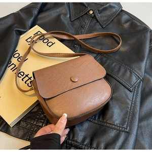 Detailed macro view of brown faux leather crossbody bag with classic litchi texture and button