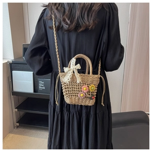 Detail of straw crossbody bag with floral accents and lace bow on a black dress