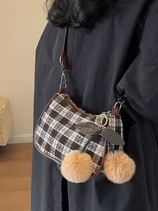 Brown and white tweed crossbody bag with a large cherry plush charm on a model's shoulder