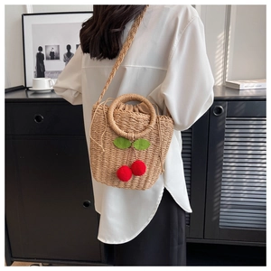 Detail view of woven straw shoulder bag with red pompom cherry accents and drawstring liner