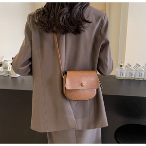 Close-up of a brown vintage leather saddle bag worn cross-body with a sleek round buckle