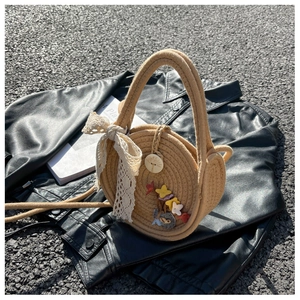 Détail d'un sac en paille rond avec broderie florale et nœud en dentelle sur cuir