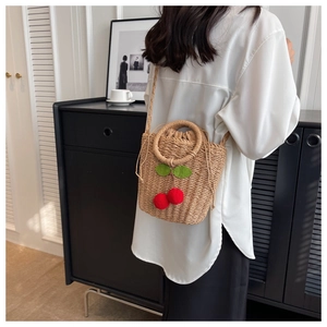 Detail of straw bucket bag with red cherry accents and drawstring closure worn by model