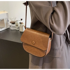 Detail of a brown vintage saddle bag with荔枝 texture and round clasp on a model