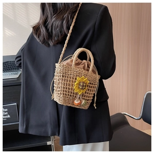 Model wearing a hand-woven straw bucket bag with sunflower charm and drawstring liner