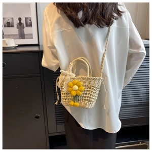 Detail view of a woven straw bag with hollow knit patterns and a yellow flower pendant