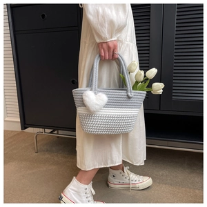 Detail der handgewebten Streifen-Eimertasche mit weißem Herz-Plüschanhänger und Griff
