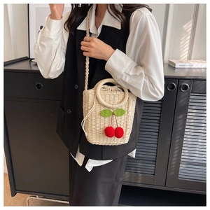 Detailed view of beige straw bucket bag with red cherry poms and drawstring closure