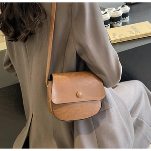 Close-up of a brown vintage saddle bag with crackle texture on a dark blazer