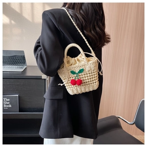 Detail of straw woven bucket bag featuring knitted cherry charms and drawstring liner