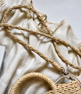 Detail of hand-woven cream straw bag showing braided shoulder strap and silver metal hooks