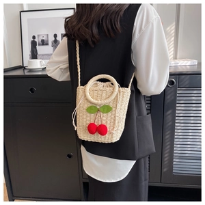 Detail of mini straw crossbody bag with red cherry accents and drawstring closure
