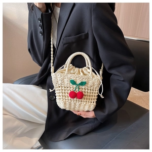 Detail of hand-woven straw beach bag featuring knitted cherry charms and drawstring lining