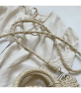 Detail of hand-woven straw bag featuring beige braided straps and silver metal buckles