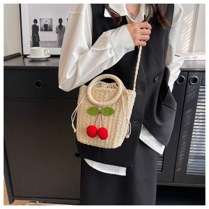 Detail of straw woven crossbody bag with red cherry accents and a drawstring lining