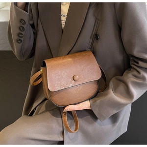Detail of a brown leather saddle bag with lychee texture worn over a stylish blazer