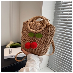 Detailed close-up of handmade straw bucket bag with 3D cherry accents and round handle