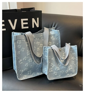 Detail of light blue floral jacquard tote bag set with wide woven straps on a black sofa