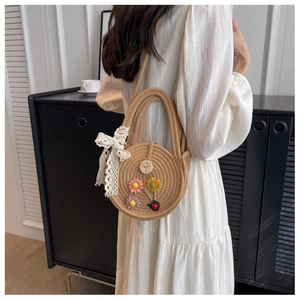 Detail der Strohtasche mit Blumen-Patches und Spitzenschleife am Modell in weißem Kleid