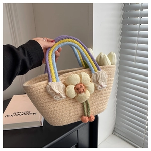 Detail of handwoven bag with rainbow handles, floral accent, and plush ball charms