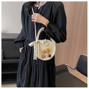 Detail einer runden beigen Strohtasche mit Blumen und Spitzenschleife an einem Model