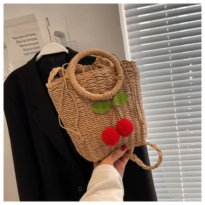 Close-up of woven straw handbag featuring 3D red cherry accents and drawstring lining