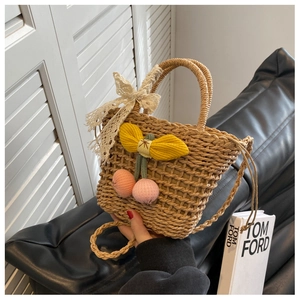 Detail of hand-woven straw bag with lace bow, cherry charms and textured finish