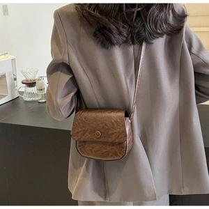 Brown vintage saddle bag with crinkled texture worn over a dark blazer for a chic look