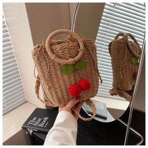 Detail of straw woven bag with red cherry accents and ring handle in a summer setting