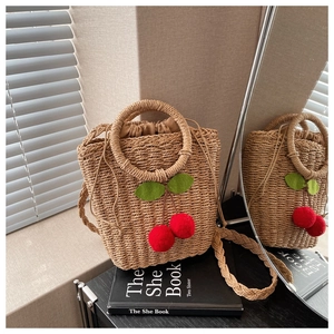 Detail of woven straw bag featuring 3D red cherry accents and drawstring inner pouch